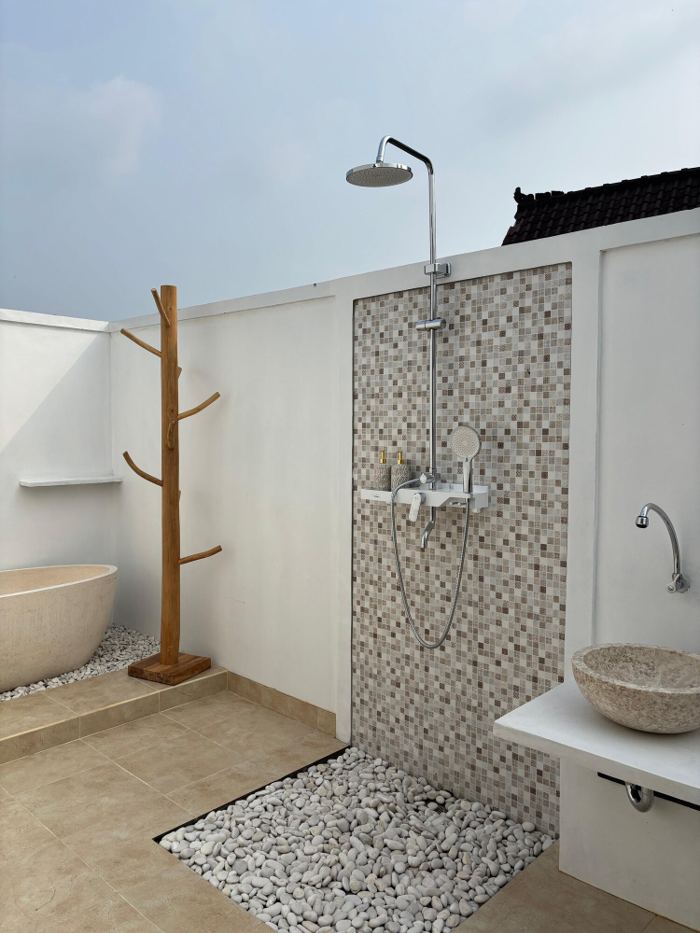 Open-air shower area with a stone bathtub, mosaic wall and pebble floor