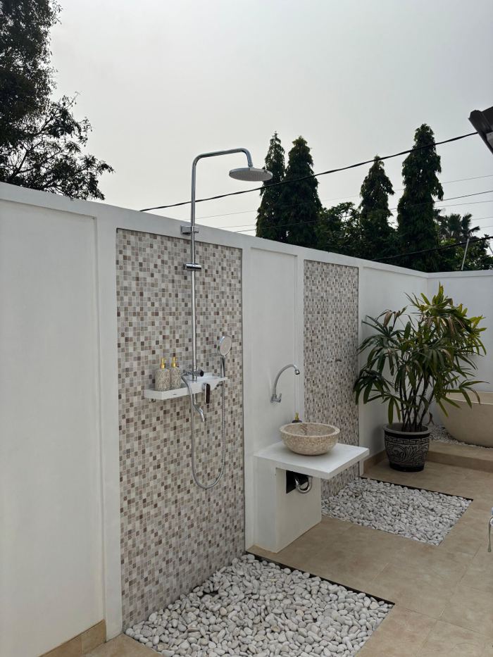 Outdoor shower with a stone basin, potted palm and white pebbles
